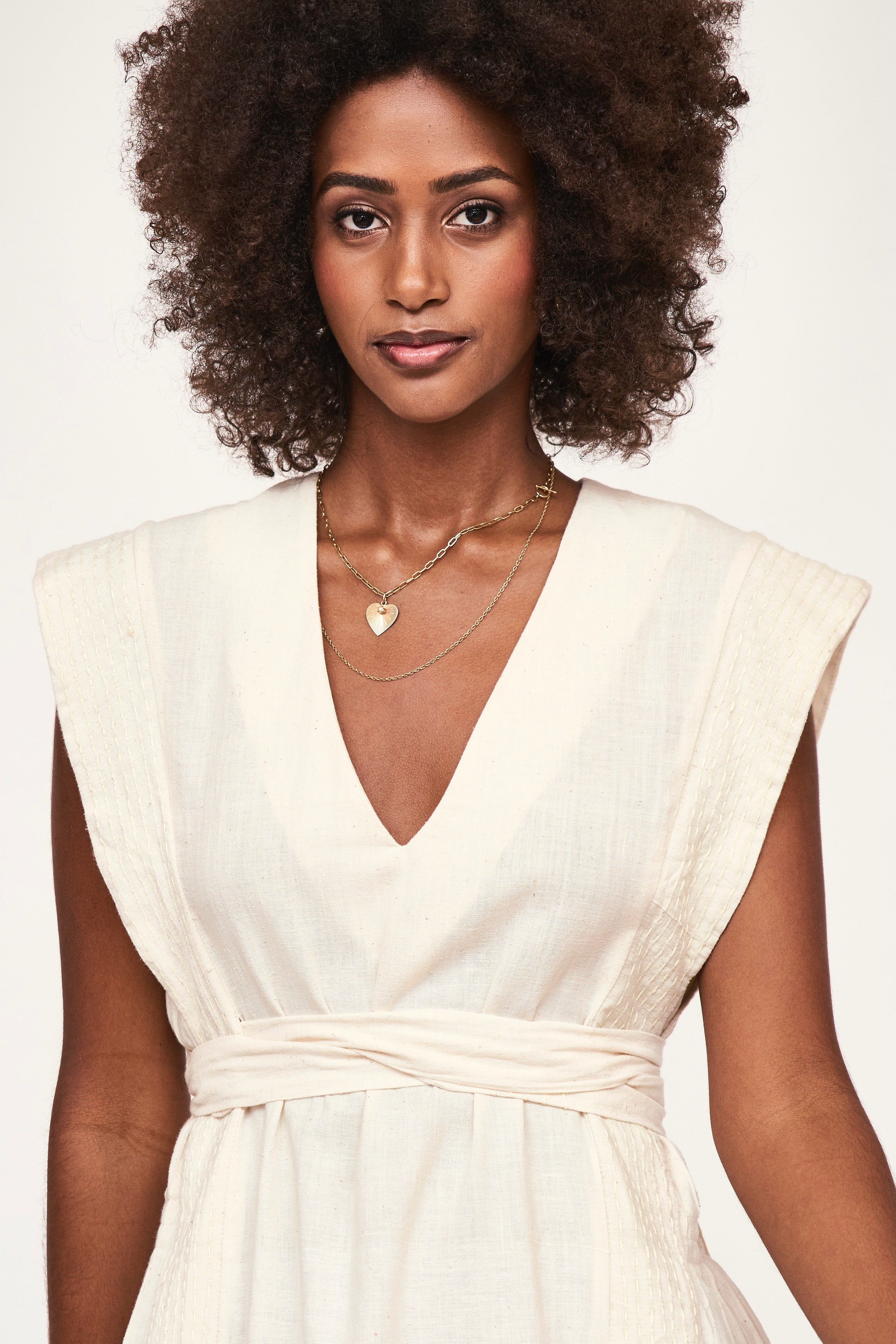 Girl wearing MIRTH women's v neck layered pintuck sleeveless long belted laguna dress in parchment cream cotton