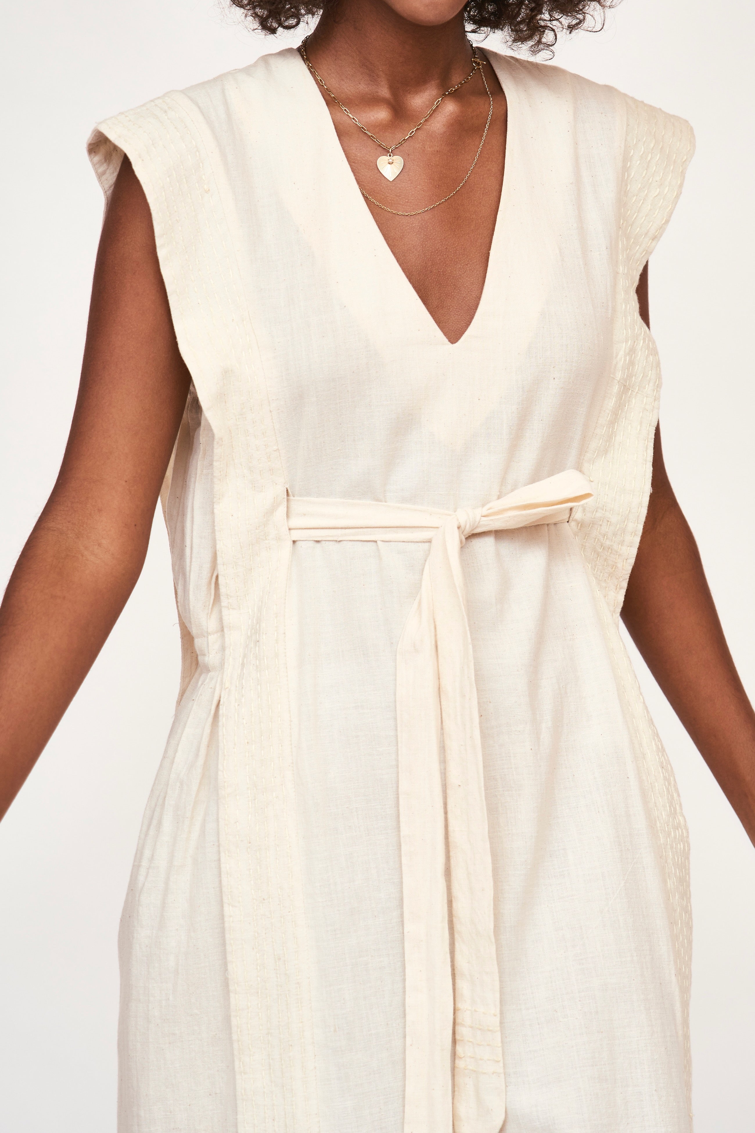 Girl wearing MIRTH women's v neck layered pintuck sleeveless long belted laguna dress in parchment cream cotton