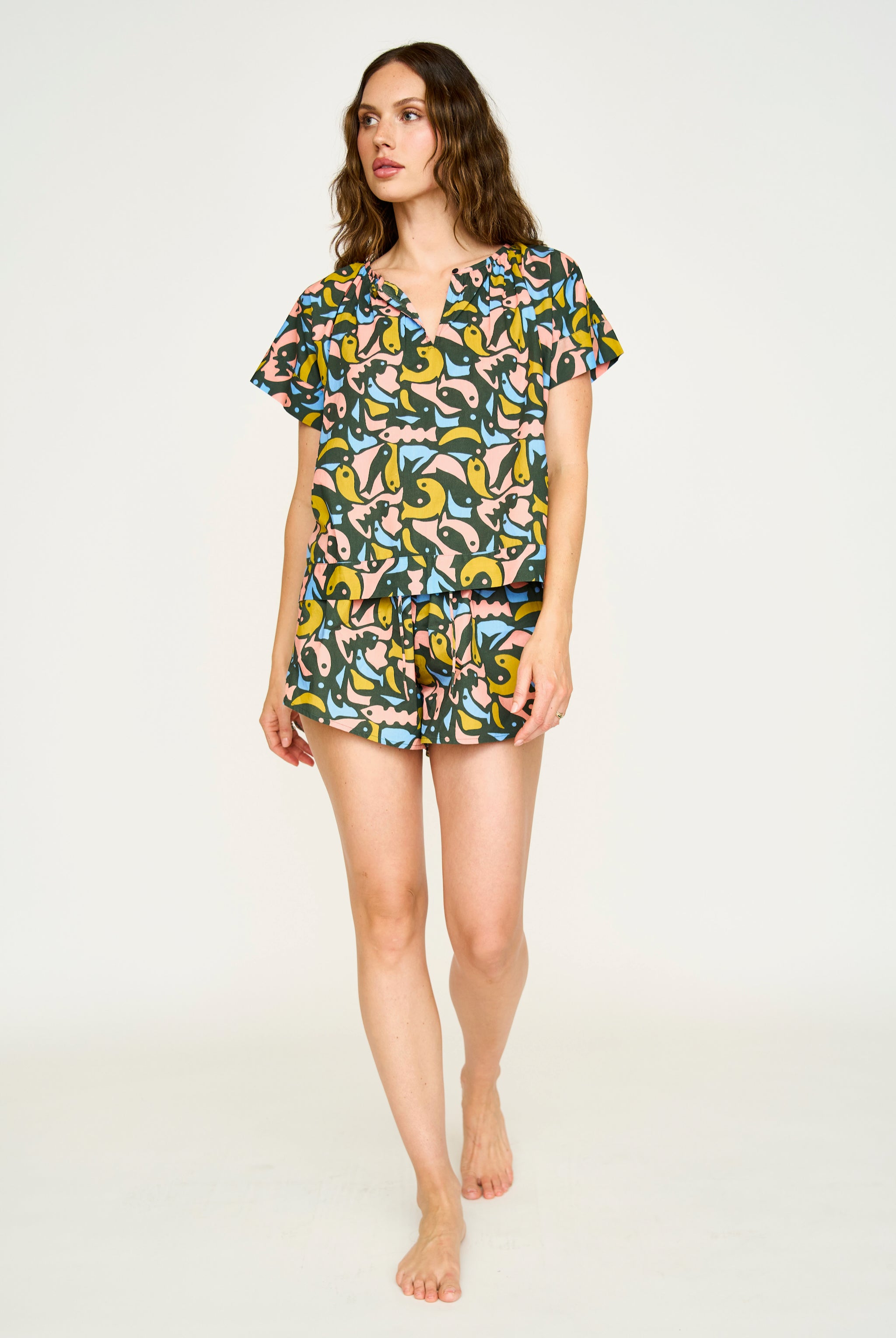 A woman standing, wearing a short-sleeved cotton pajama set with a guppy pattern and a soft elastic waistband. The set includes pajama shorts with a wide leg opening.