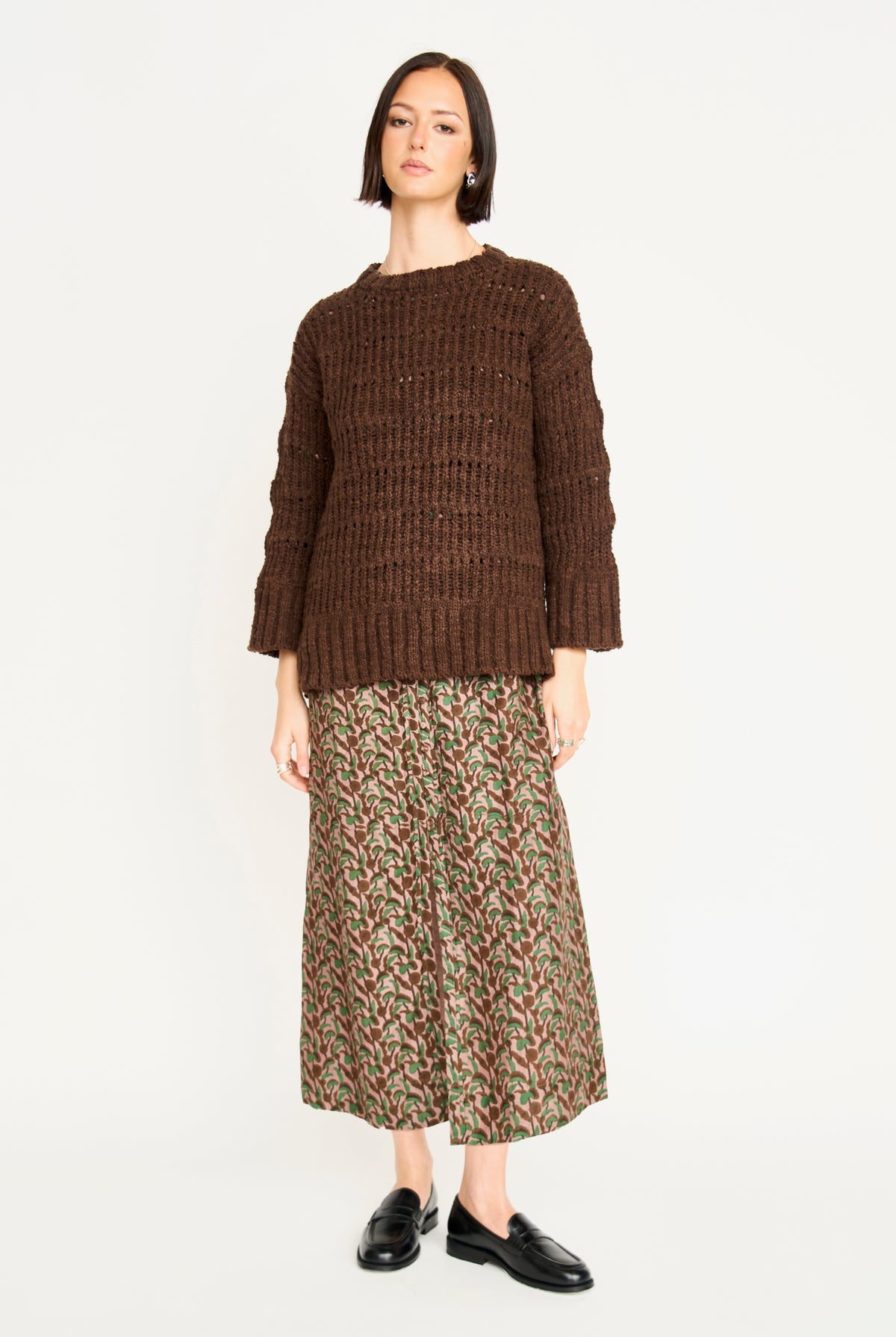 Woman wearing a brown knitted sweater and patterned skirt on a white background