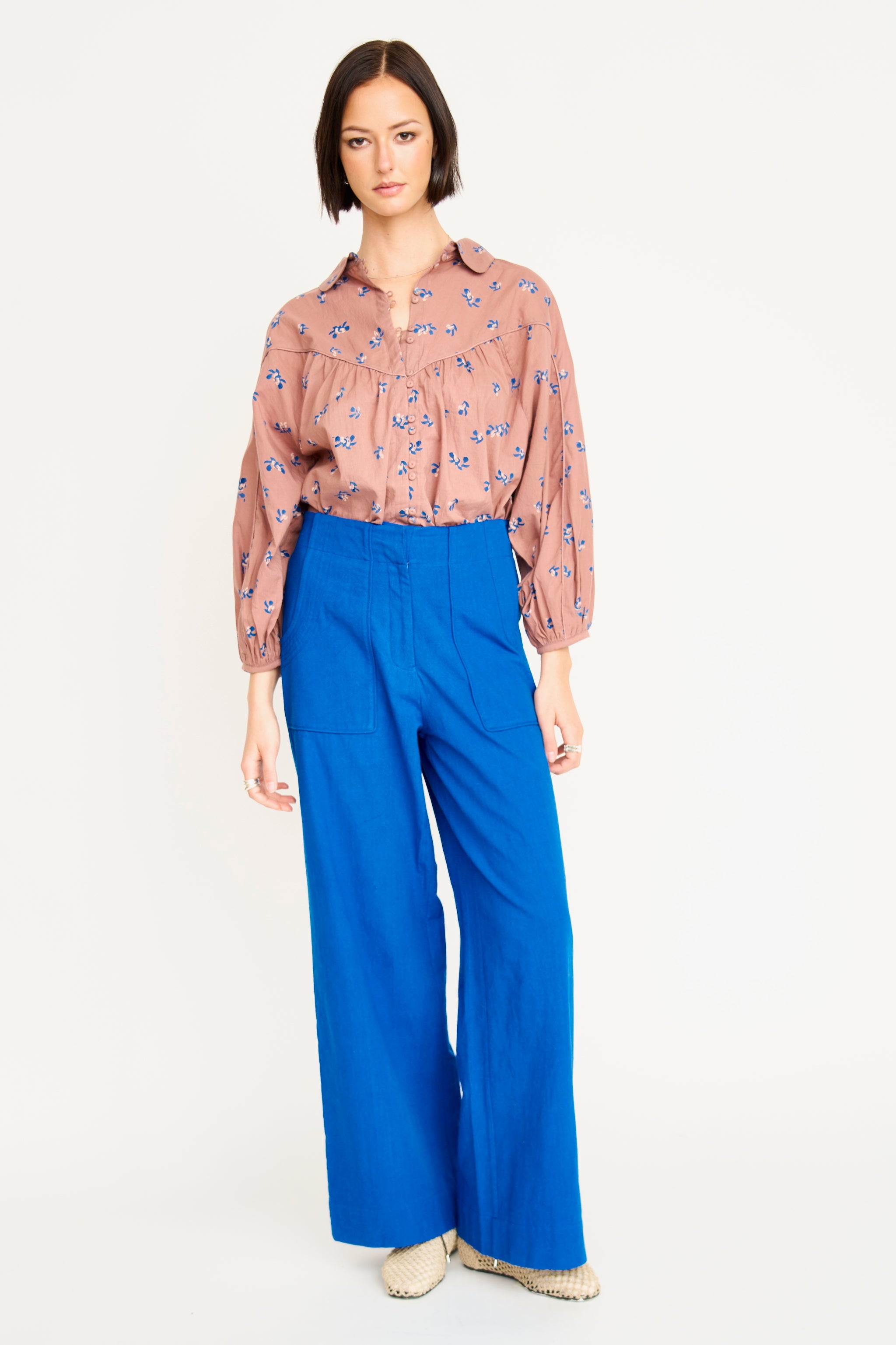 Woman wearing a patterned blouse and blue pants on a white background