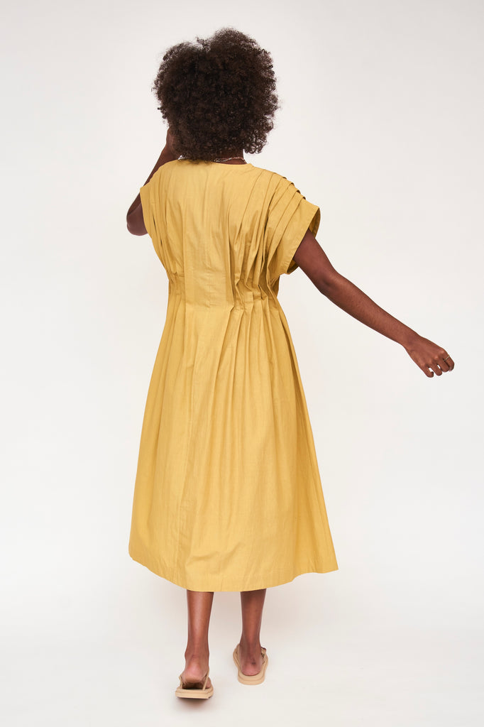 Girl wearing MIRTH women's midi v neck pleated korcula dress in gilded yellow cotton