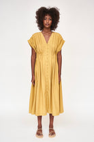 Girl wearing MIRTH women's midi v neck pleated korcula dress in gilded yellow cotton