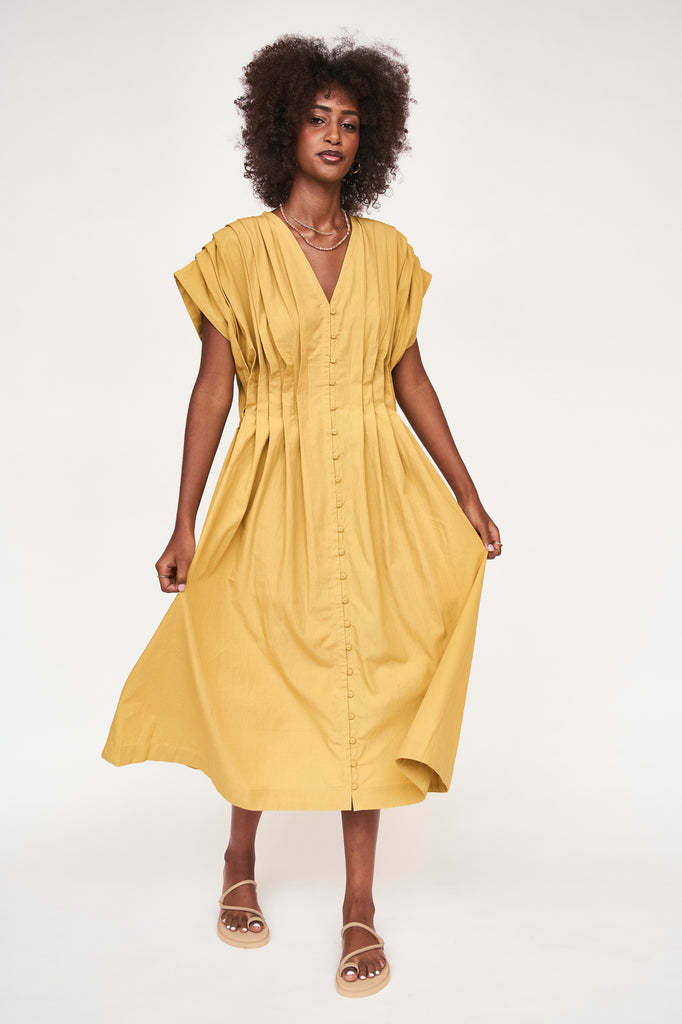 Girl wearing MIRTH women's midi v neck pleated korcula dress in gilded yellow cotton