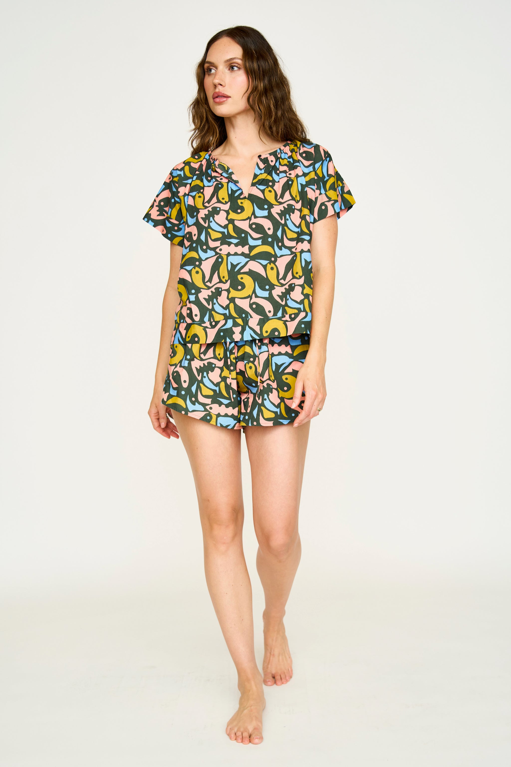 A woman standing, wearing a short-sleeved cotton pajama set with a guppy pattern and a soft elastic waistband. The set includes pajama shorts with a wide leg opening.