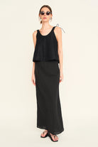 Woman wearing a black sleeveless top and long skirt on a white background