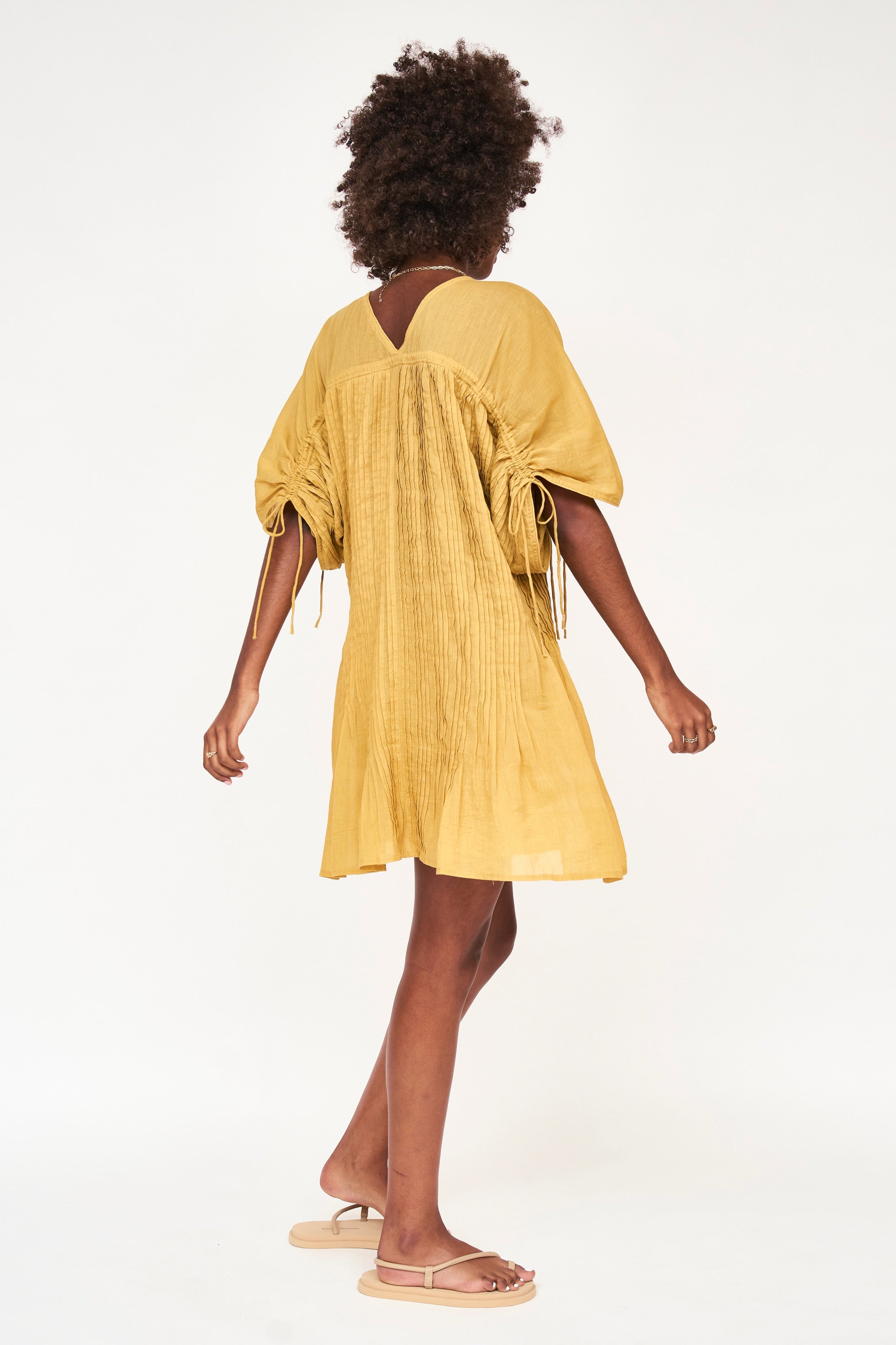 Girl wearing MIRTH women's v neck pleated pull string malta lined coverup short dress in gilded yellow cotton