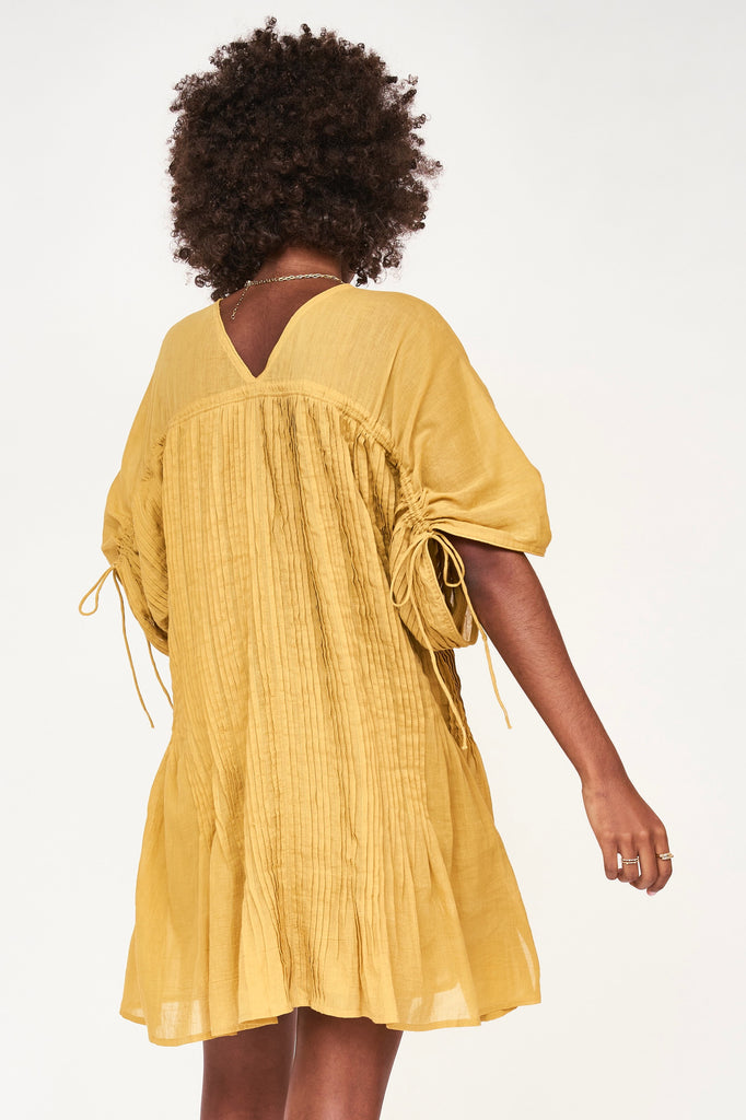 Girl wearing MIRTH women's v neck pleated pull string malta lined coverup short dress in gilded yellow cotton