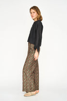 A woman modeling a black long-sleeve blouse and wide-leg patterned trousers with a beige woven slip-on shoe, photographed against a plain white studio background.