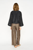 A woman viewed from the back wearing a black long-sleeve cropped top and patterned wide-leg trousers with a beige flat sandal, set against a plain white studio background.